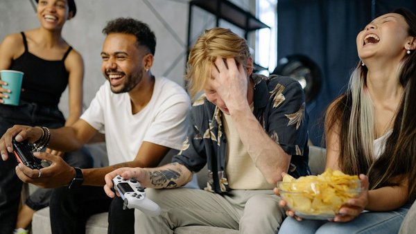 Conseils pour une cohabitation harmonieuse Quatre jeunes personnes assises sur un canapé rient en jouant à un jeu vidéo
