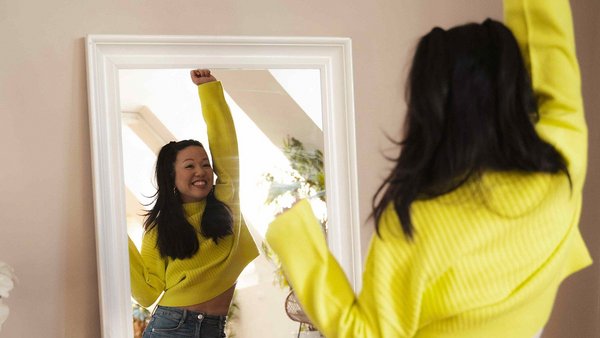 Pourquoi faire un semestre à l’étranger ? Une femme en pull jaune étire ses bras devant le miroir