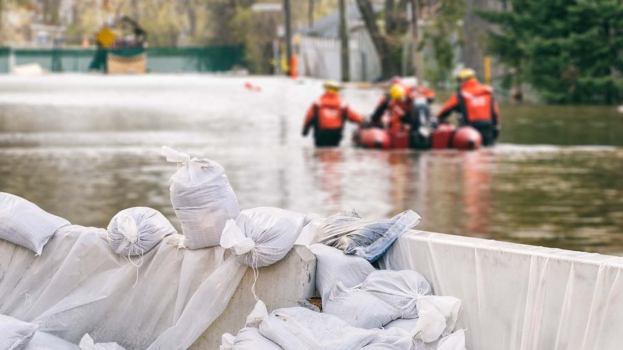 Les dégâts causés par les intempéries et leurs conséquences financières Des maisons inondées protégées par des sacs de sable et une équipe de secours en arrière-plan